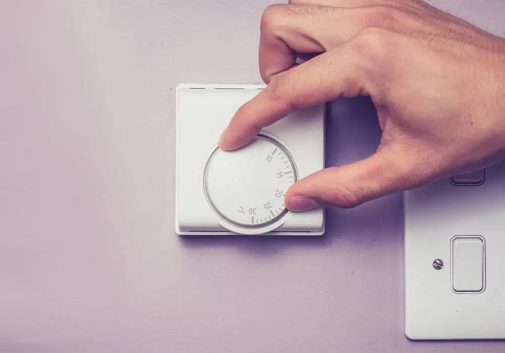 Man turning down the temperature on a room thermostat