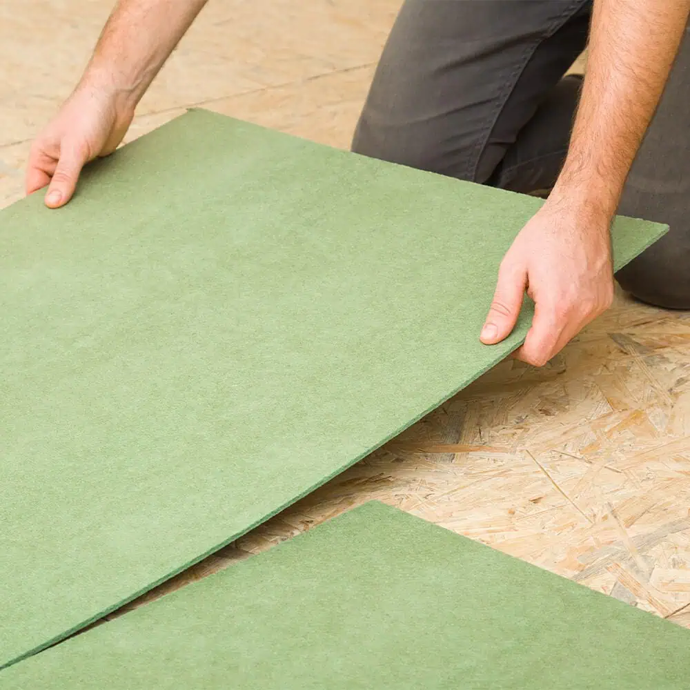 Man laying a fibreboard underlay over an osb subfloor ready for laminate flooring