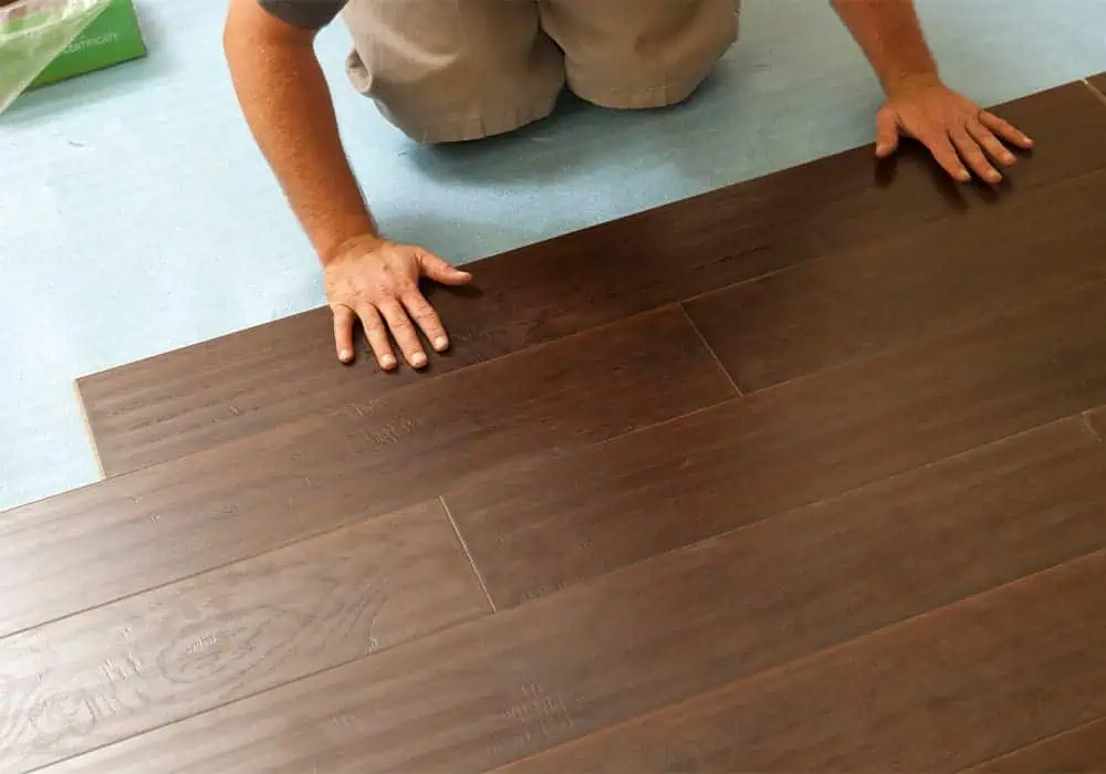 Man laying laminate flooring planks over a foam underlay