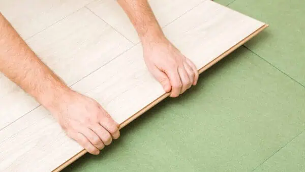 Man installing laminate flooring over the top of green fibreboardunderlay