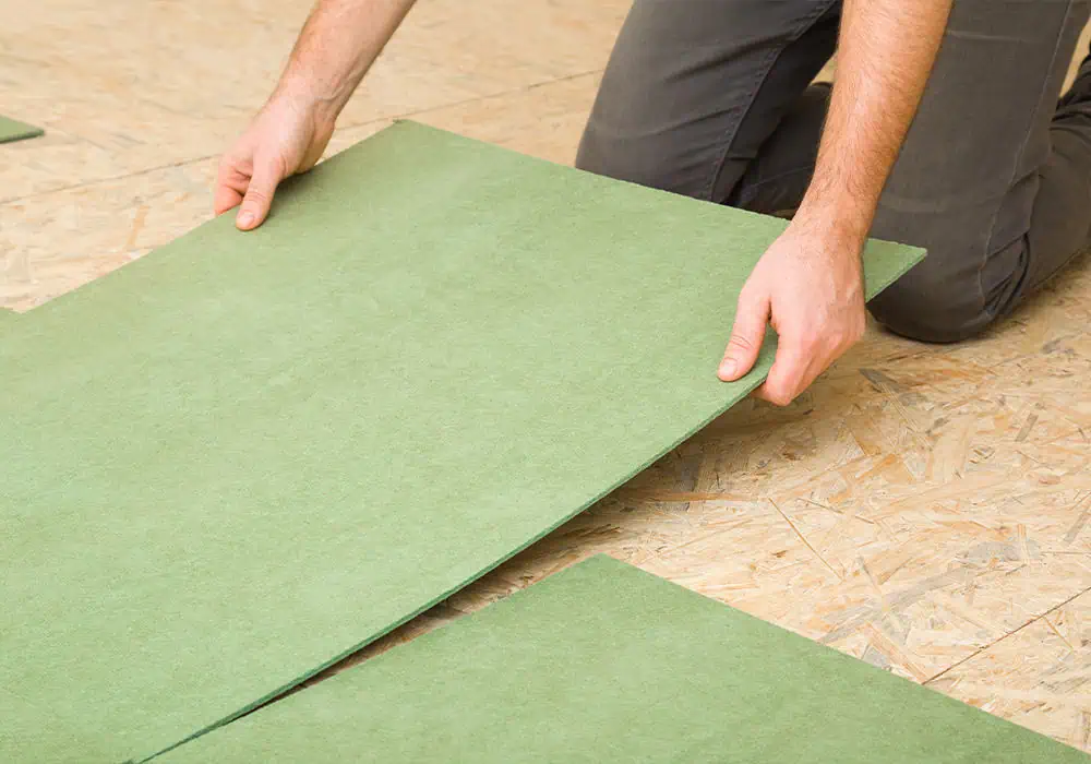 Man laying fibreboard underlay over a wooden subfloor