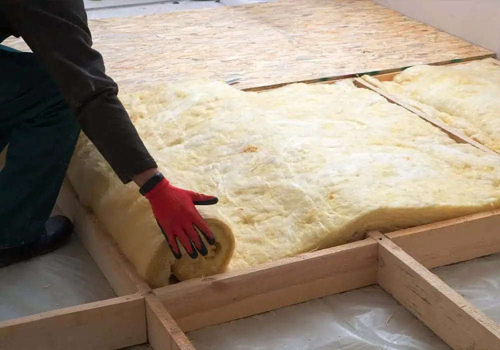 Man installing rockwool insulation between flooring joists to improve soundproofing and thermal loss