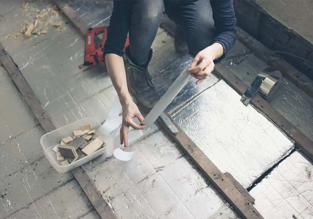 Woman insulating a suspended timber floor using PIR insulation board and silver tape