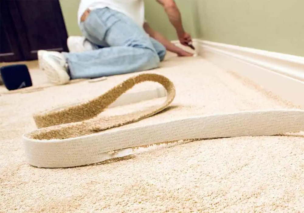 Man trimming the edge of a carpet with a stanley knife to size for fitting