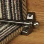 Jubilee Stair Carpet Runner Rod in pewter installed on wooden stairs with a striped runner