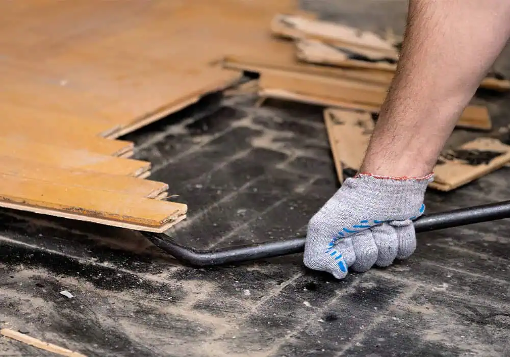 Man clearing old laminate flooring from a room using a crowbar