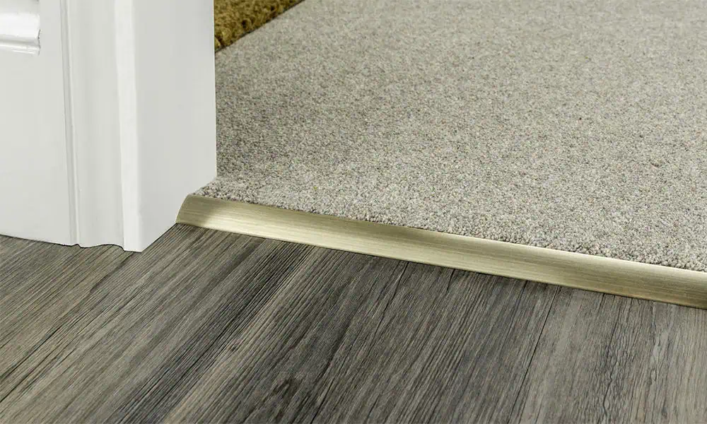 Single edge door bar in satin brass transitioning from carpet to laminate