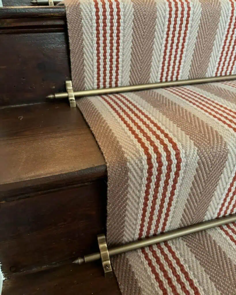 Close up of a striped carpet runner with antique brass stair rods